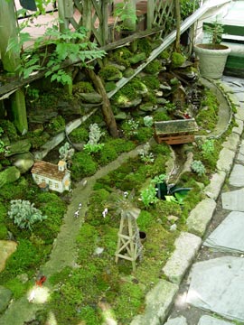 A working train runs through this miniature village that uses moss to simulate grassy fields.